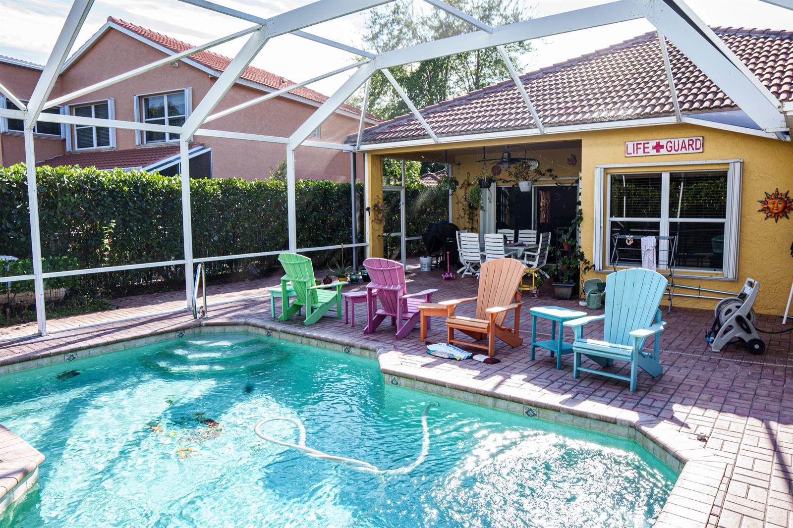 A screened-in patio features a swimming pool, colorful Adirondack chairs, and a yellow exterior wall — 8058 Via Hacienda, Riviera Beach FL 33418, RIVIERA BEACH, FL
