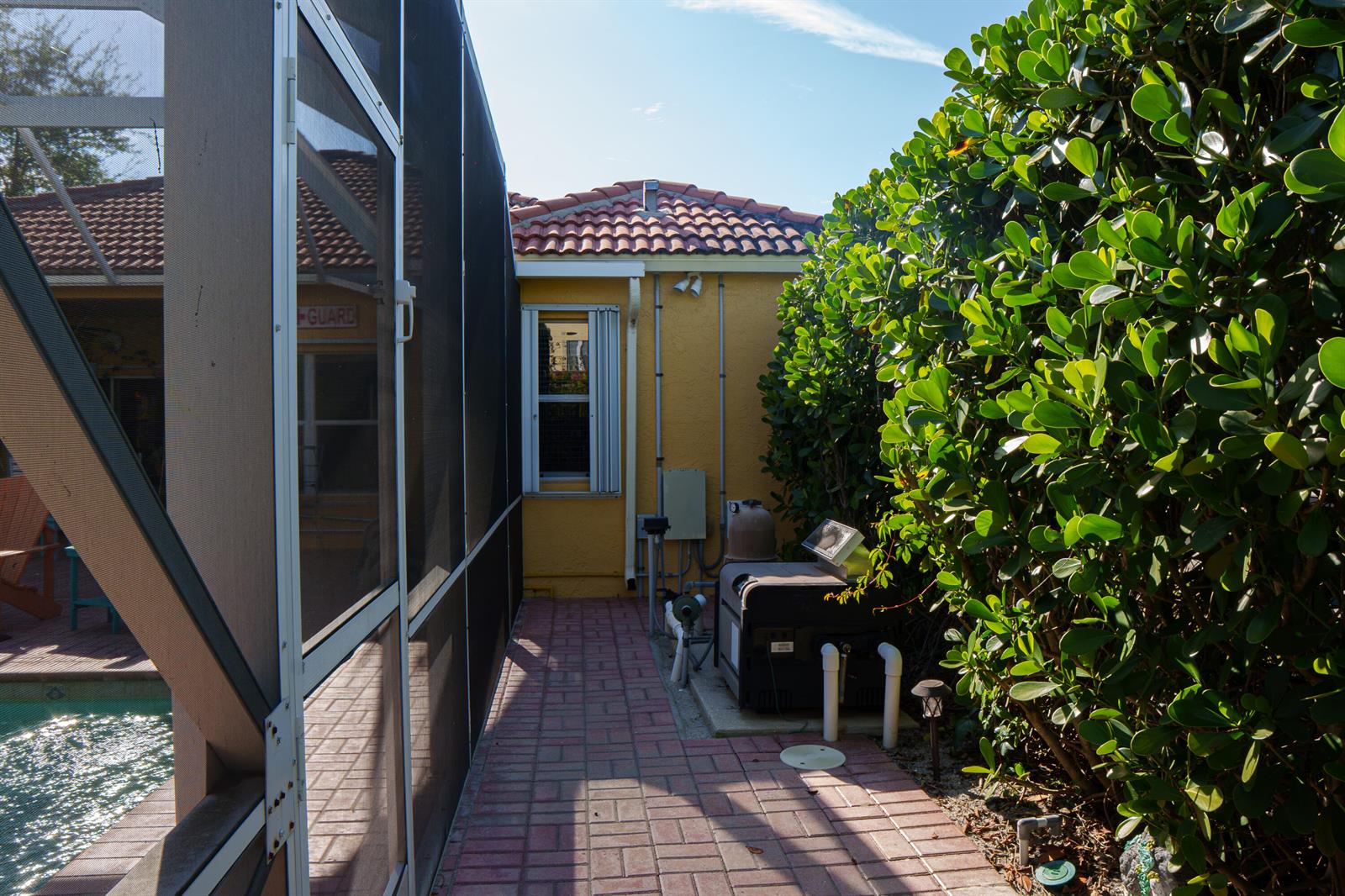A brick walkway runs between a screened pool enclosure and a yellow house exterior — 8058 Via Hacienda, Riviera Beach FL 33418, RIVIERA BEACH, FL