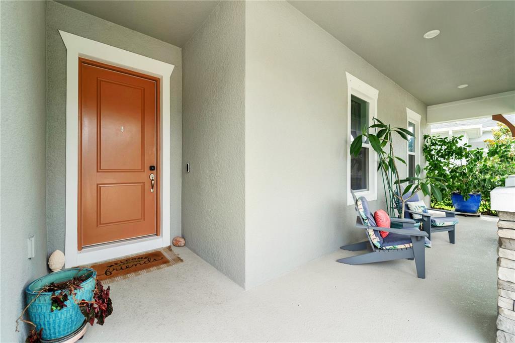 A covered front porch features a terracotta-colored door, two wooden chairs, and potted plants — 16429 FREHLEY RUN, LAND O LAKES, FL