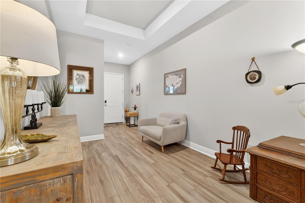 A bright entryway features light wood-look flooring, a tray ceiling, and a small seating area — 16429 FREHLEY RUN, LAND O LAKES, FL