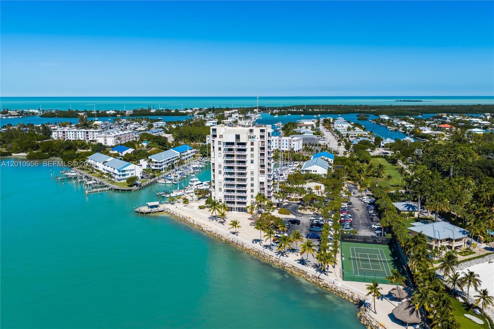 An aerial view shows a tall residential building surrounded by a marina, parking, and tennis courts — 2000 Coco Plum Dr # 601, Marathon FL 33050, MARATHON, FL