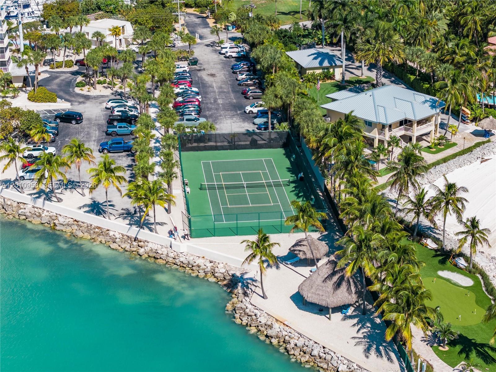 An aerial view shows a tennis court, parking lot, and beach area with tiki huts — 2000 Coco Plum Dr # 601, Marathon FL 33050, MARATHON, FL
