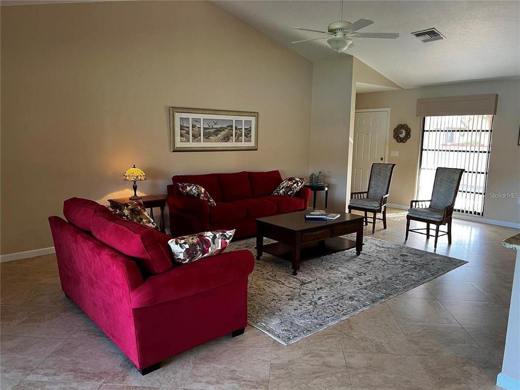 A living room features red sofas, a coffee table, and a rug on tile flooring — 5581 GOLF POINTE DRIVE, SARASOTA, FL