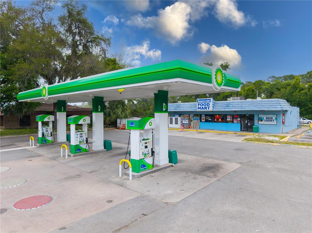 A gas station with a green canopy, fuel pumps, and a blue convenience store building — 487 S US 301, SUMTERVILLE, FL