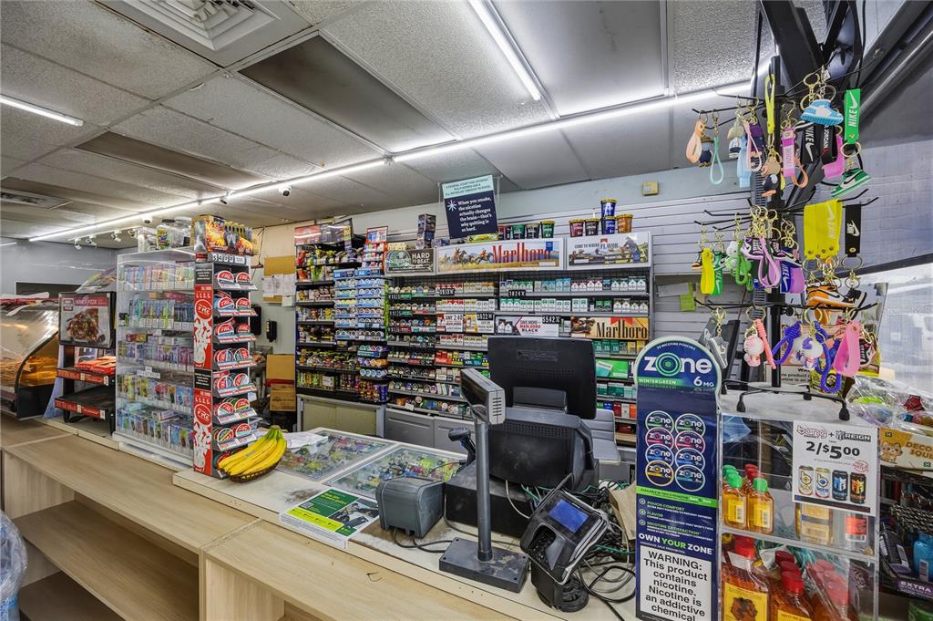 A convenience store counter features shelves stocked with tobacco products, snacks, and hanging keychains — 487 S US 301, SUMTERVILLE, FL