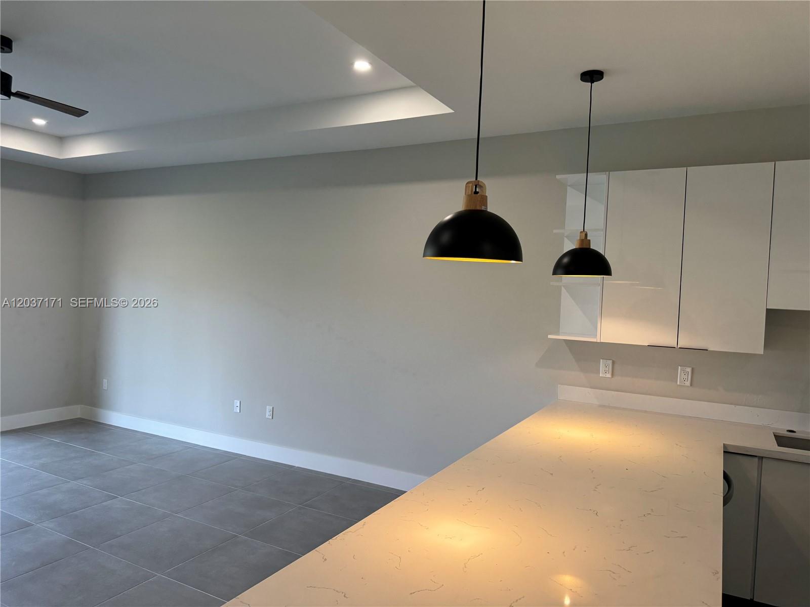 A kitchen features a white quartz countertop, two black pendant lights, and gray tile flooring — LEHIGH ACRES, FL