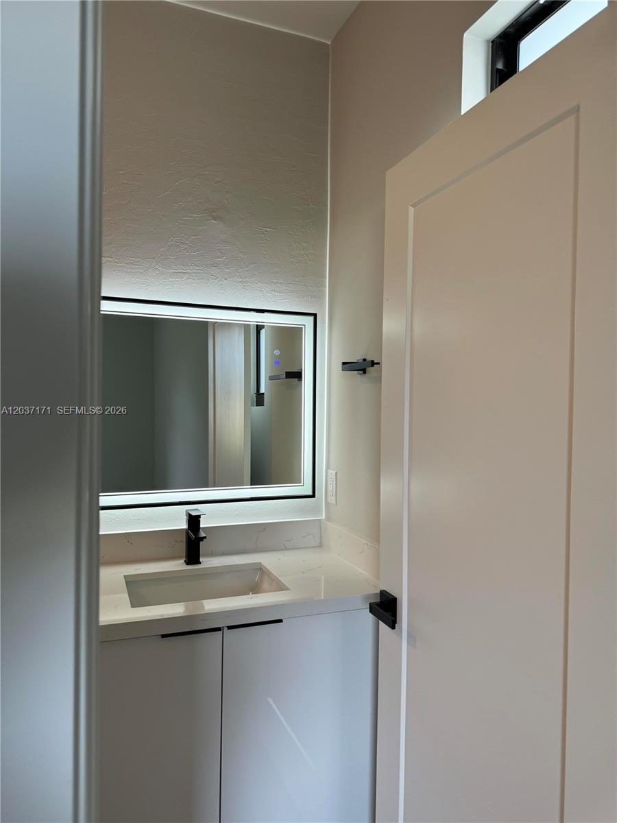 A modern bathroom features a white vanity, a backlit mirror, and matte black hardware — LEHIGH ACRES, FL