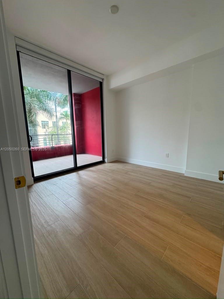 An empty room features light wood-look flooring, white walls, and a sliding glass door to a balcony — 90 NE 32 ST # 206, Miami FL 33137, MIAMI, FL