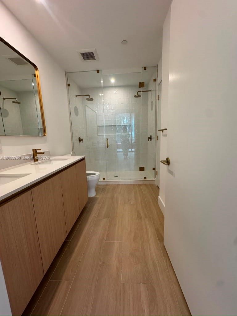 A modern bathroom features a double vanity, wood-look tile flooring, and a glass-enclosed walk-in shower — 90 NE 32 ST # 206, Miami FL 33137, MIAMI, FL