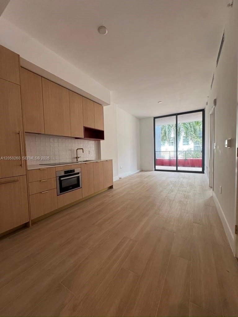 A modern kitchen with light wood cabinetry and stainless steel appliances opens to a balcony — 90 NE 32 ST # 206, Miami FL 33137, MIAMI, FL
