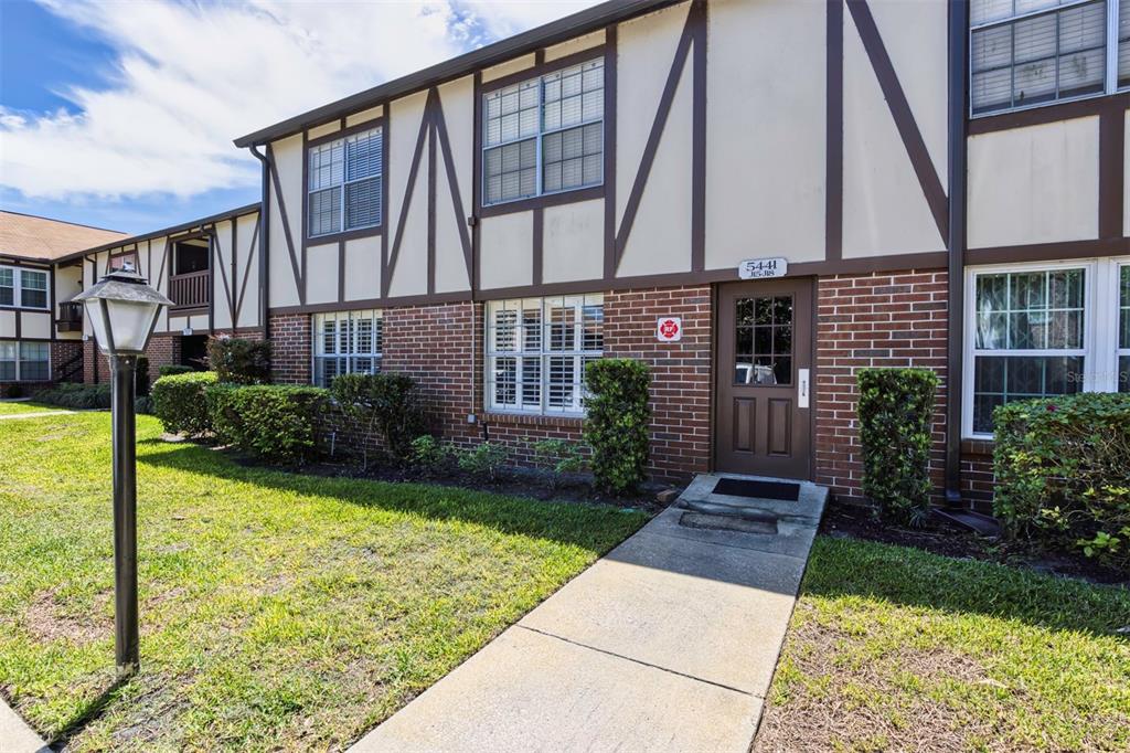 A two-story apartment building exterior features brick siding, timber framing, and a concrete walkway — 5441 HANSEL AVENUE UNIT J15, ORLANDO, FL