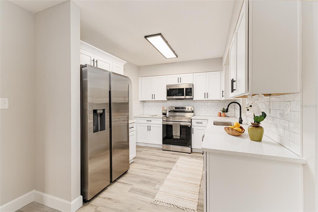 A modern kitchen features white cabinets, stainless steel appliances, and light wood-look flooring — 1955 CAPPS ROAD, LAKE WALES, FL