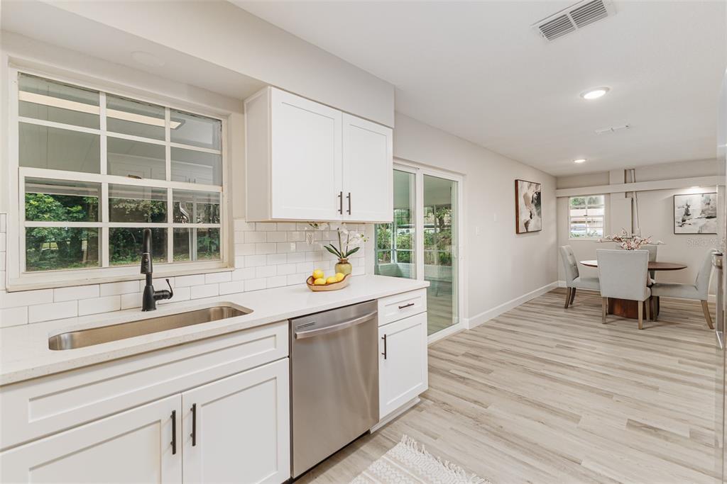 A kitchen with white cabinets, a stainless steel dishwasher, and a dining area beyond — 1955 CAPPS ROAD, LAKE WALES, FL