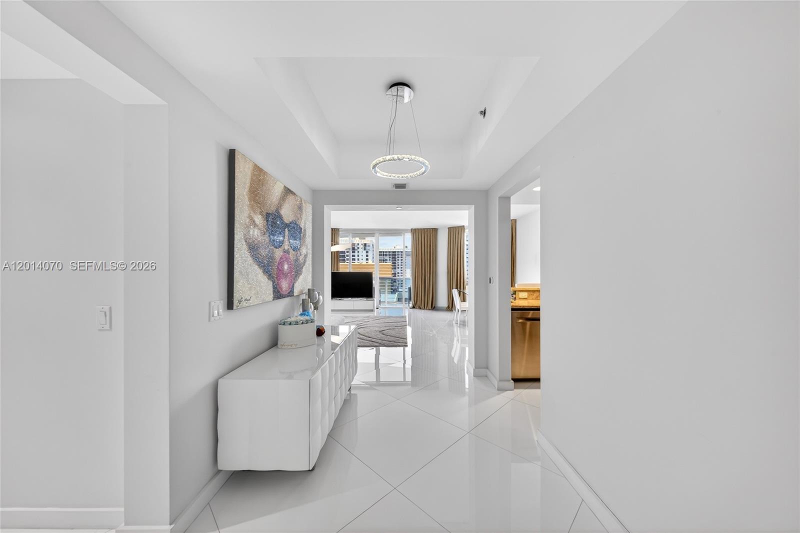 A white-tiled hallway leads to a living area with a modern chandelier and artwork — 2711 S Ocean Dr # 1901, Hollywood FL 33019, HOLLYWOOD, FL