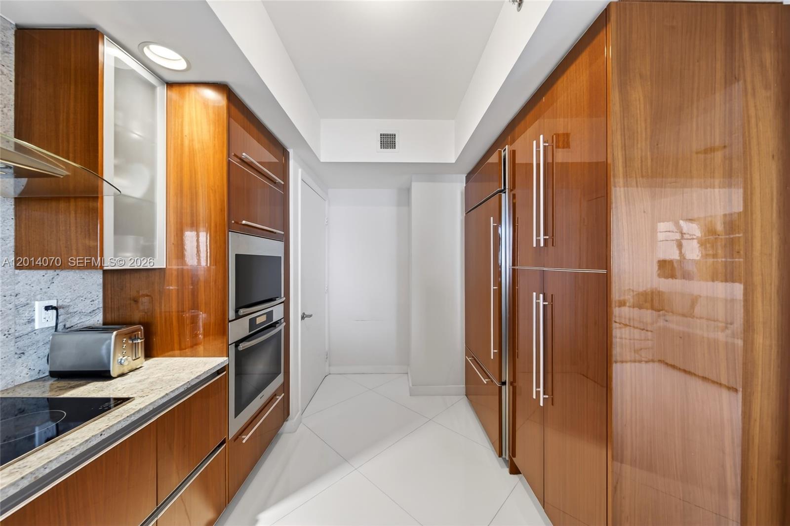 A modern galley kitchen features glossy wood cabinetry, stainless steel appliances, and white tile flooring — 2711 S Ocean Dr # 1901, Hollywood FL 33019, HOLLYWOOD, FL