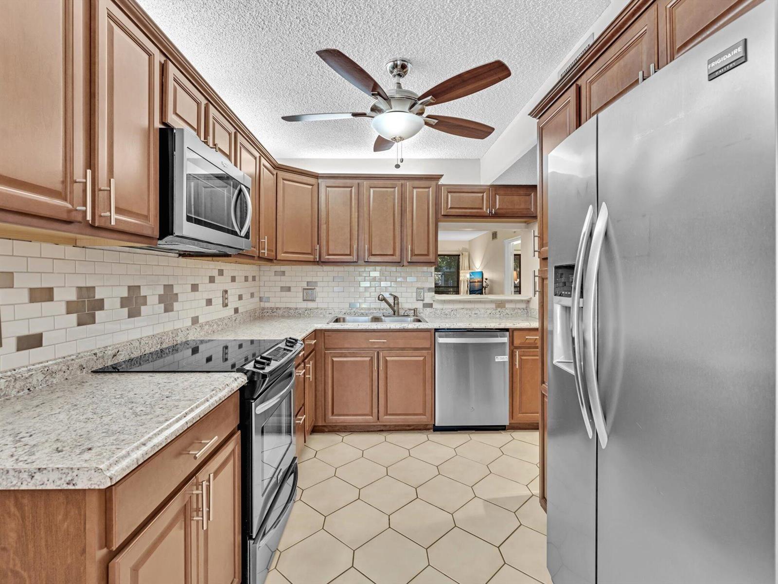 A kitchen with wood cabinets, stainless steel appliances, granite countertops, and a hexagonal tile floor — 10143 Mangrove Drive # 203, Boynton Beach FL 33437, BOYNTON BEACH, FL