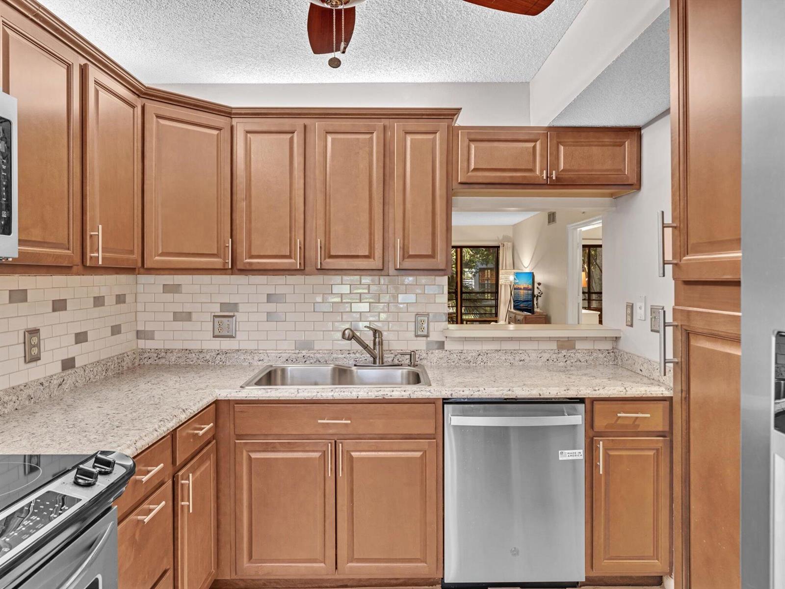 A kitchen with wood cabinets, granite countertops, a stainless steel dishwasher, and a tiled backsplash — 10143 Mangrove Drive # 203, Boynton Beach FL 33437, BOYNTON BEACH, FL