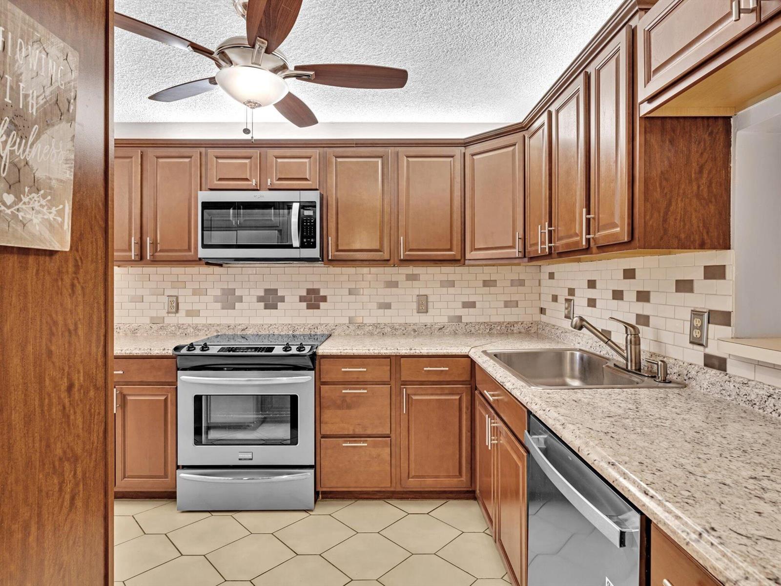 A kitchen features wood cabinets, stainless steel appliances, granite countertops, and a tiled backsplash — 10143 Mangrove Drive # 203, Boynton Beach FL 33437, BOYNTON BEACH, FL