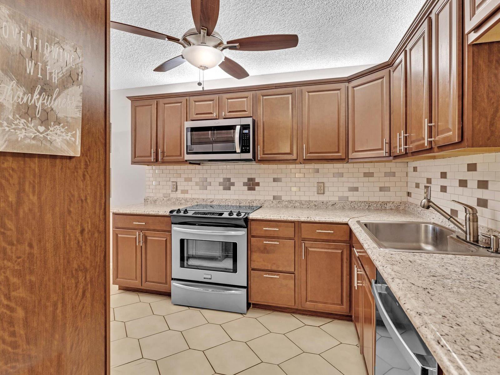A kitchen with wood cabinets, stainless steel appliances, granite countertops, and a tiled backsplash — 10143 Mangrove Drive # 203, Boynton Beach FL 33437, BOYNTON BEACH, FL