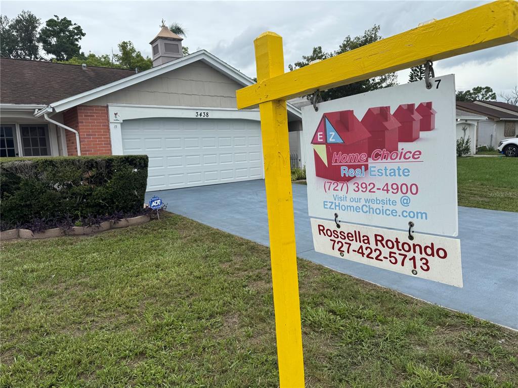 A yellow real estate sign stands in the front yard of a single-story suburban home — 3438 MOOG ROAD, HOLIDAY, FL