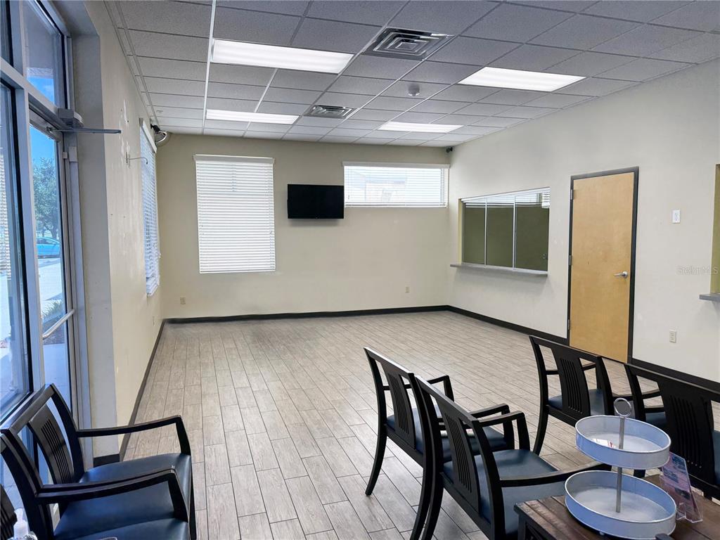 A waiting room features light wood-look tile flooring, black chairs, and a wall-mounted television — 4669 E SR 44 UNIT 102/103, WILDWOOD, FL