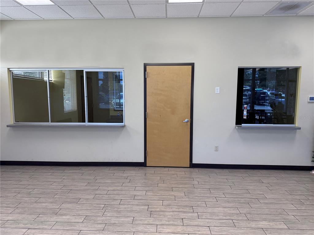 An interior room features light-colored walls, wood-look tile flooring, a central door, and two windows — 4669 E SR 44 UNIT 102/103, WILDWOOD, FL
