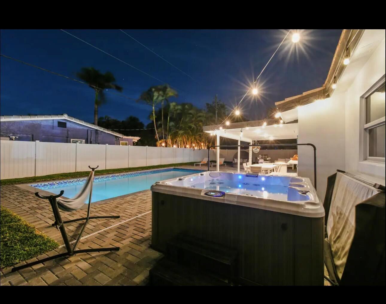 A backyard at night features a hot tub, a swimming pool, and string lights overhead — 5040 NE 22nd Avenue, Lighthouse Point FL 33064, LIGHTHOUSE POINT, FL