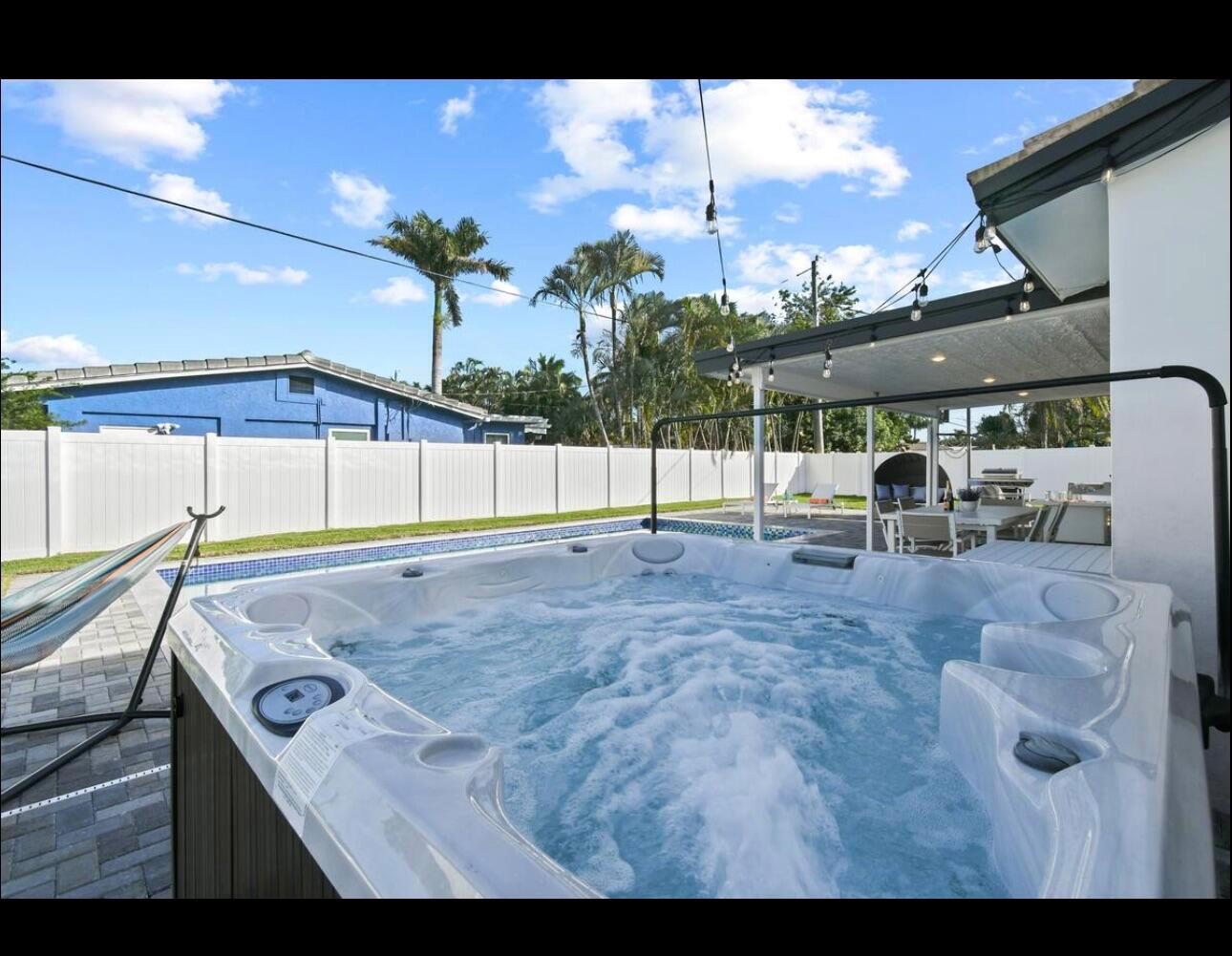 A hot tub with bubbling water sits on a paved patio next to a swimming pool — 5040 NE 22nd Avenue, Lighthouse Point FL 33064, LIGHTHOUSE POINT, FL