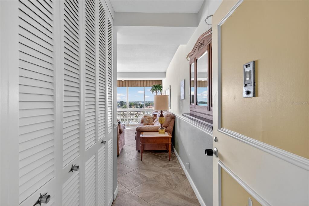 A hallway with louvered closet doors leads to a living area with a balcony view — 31 ISLAND WAY UNIT 408, CLEARWATER BEACH, FL