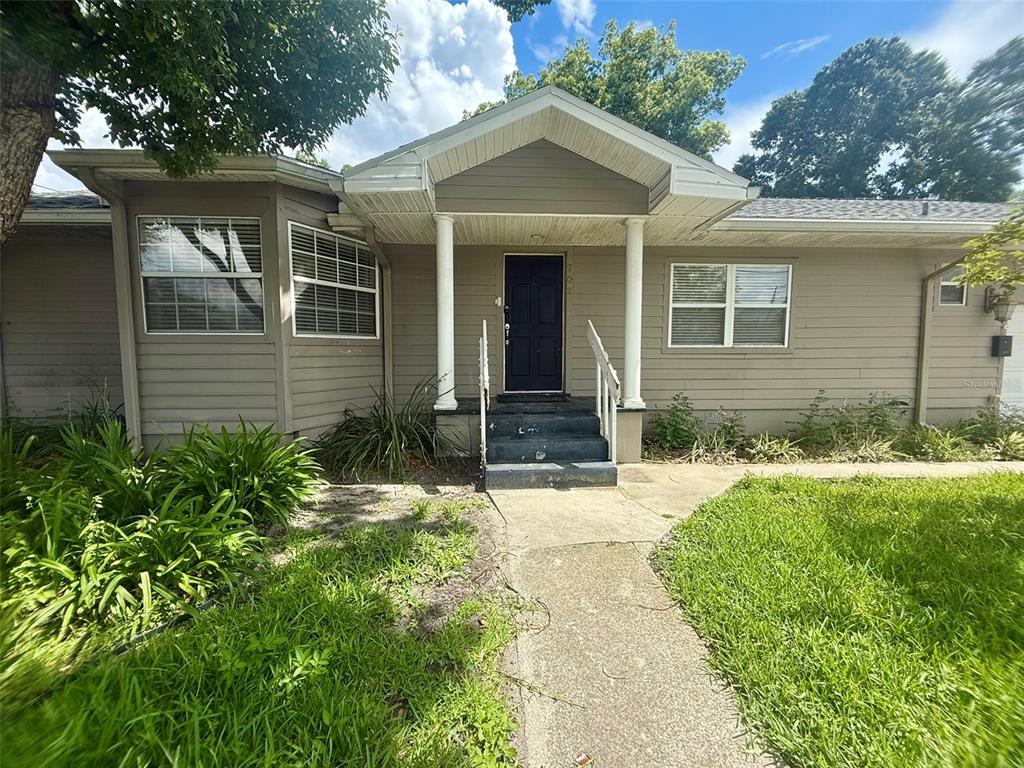 A single-story house with tan siding, a front porch, and a black front door — 702 AVENUE H NE, WINTER HAVEN, FL