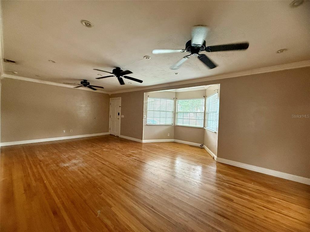 An empty living room features hardwood floors, recessed lighting, ceiling fans, and a white door — 702 AVENUE H NE, WINTER HAVEN, FL