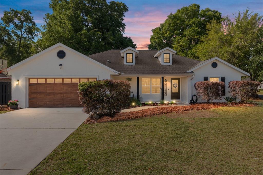 A single-story white house with a brown garage door, dormer windows, and a landscaped yard — 25175 SW 20TH AVENUE, NEWBERRY, FL