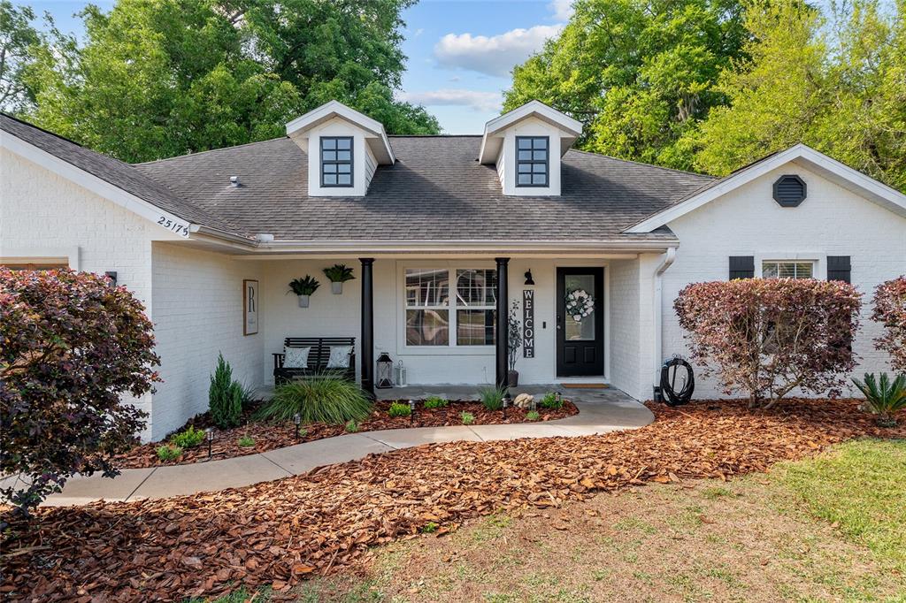A white brick house features a covered front porch, two dormer windows, and landscaping — 25175 SW 20TH AVENUE, NEWBERRY, FL