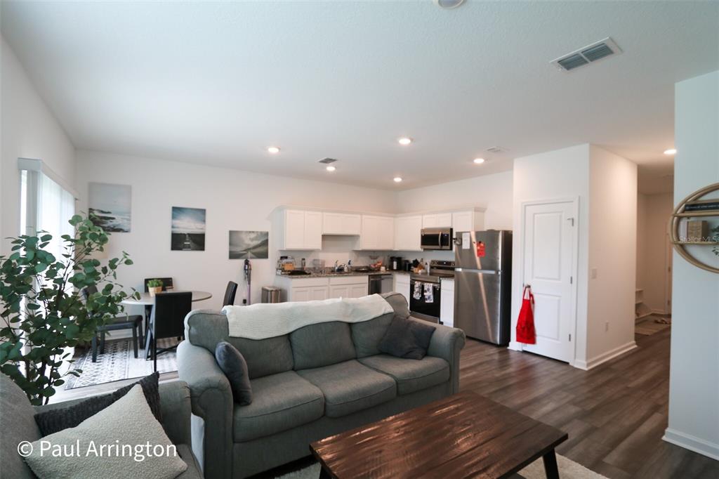 An open-concept living room and kitchen feature a gray sofa, stainless steel appliances, and wood-look flooring — 6371 KAY MORGAN LANE, GIBSONTON, FL