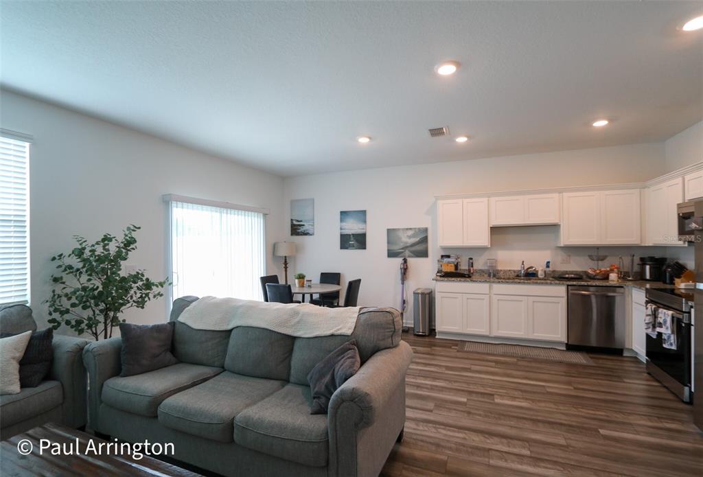 A living room and kitchen area features white cabinets, stainless steel appliances, and wood-look flooring — 6371 KAY MORGAN LANE, GIBSONTON, FL