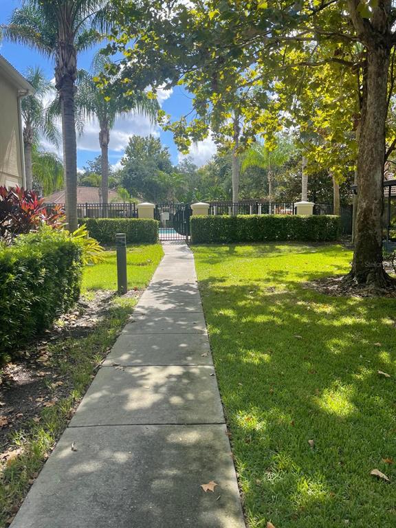 A concrete walkway leads through a grassy yard toward a gated swimming pool area — 7057 CADIZ BOULEVARD, ORLANDO, FL