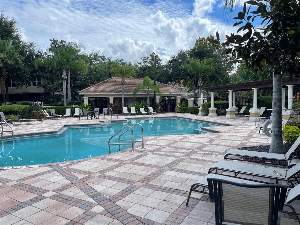 A swimming pool with lounge chairs on a paved deck in front of a clubhouse — 7057 CADIZ BOULEVARD, ORLANDO, FL