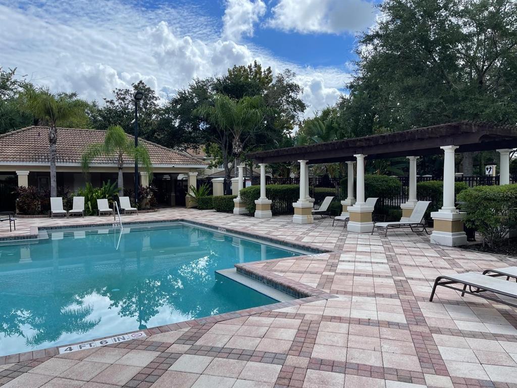 A swimming pool with a tiled deck and a covered pergola sits beside a clubhouse — 7057 CADIZ BOULEVARD, ORLANDO, FL