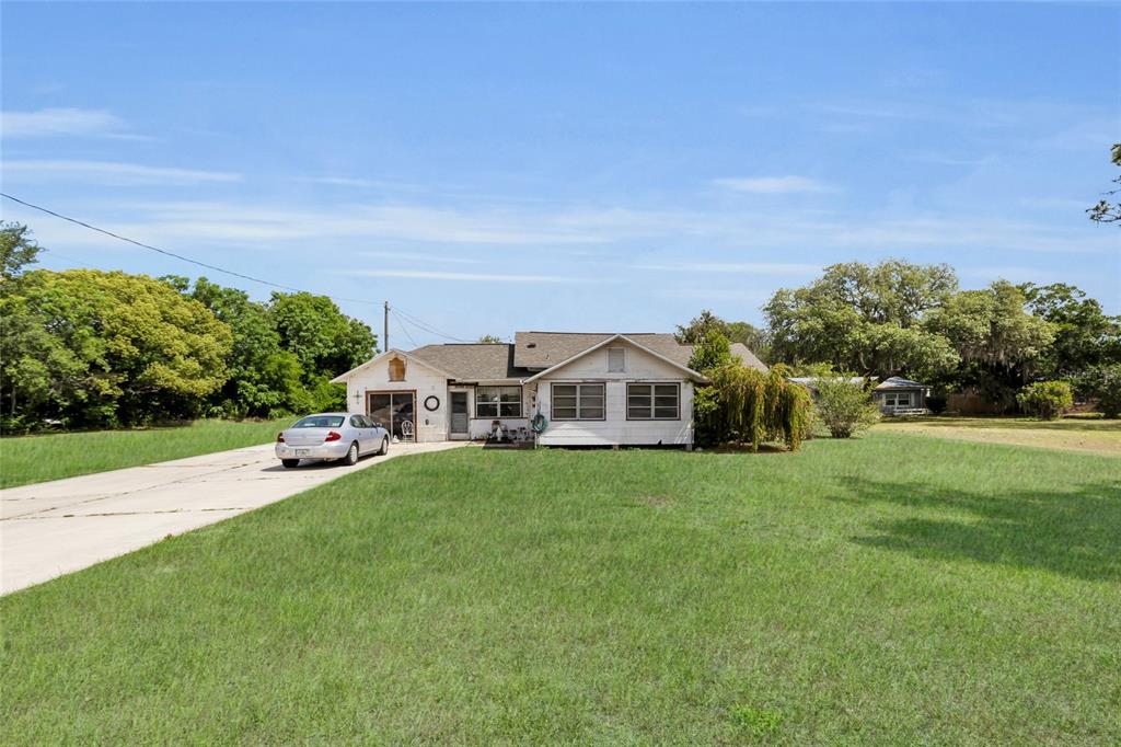 A single-story house with a white exterior, a concrete driveway, and a large grassy yard — 5223 EAGLES NEST ROAD, FRUITLAND PARK, FL
