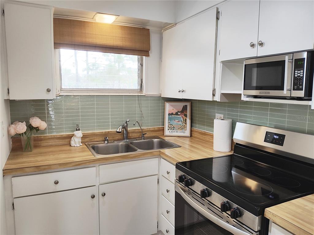 A kitchen features white cabinets, wood-look laminate countertops, a green tiled backsplash, and stainless appliances — 2155 WOOD STREET UNIT A26, SARASOTA, FL