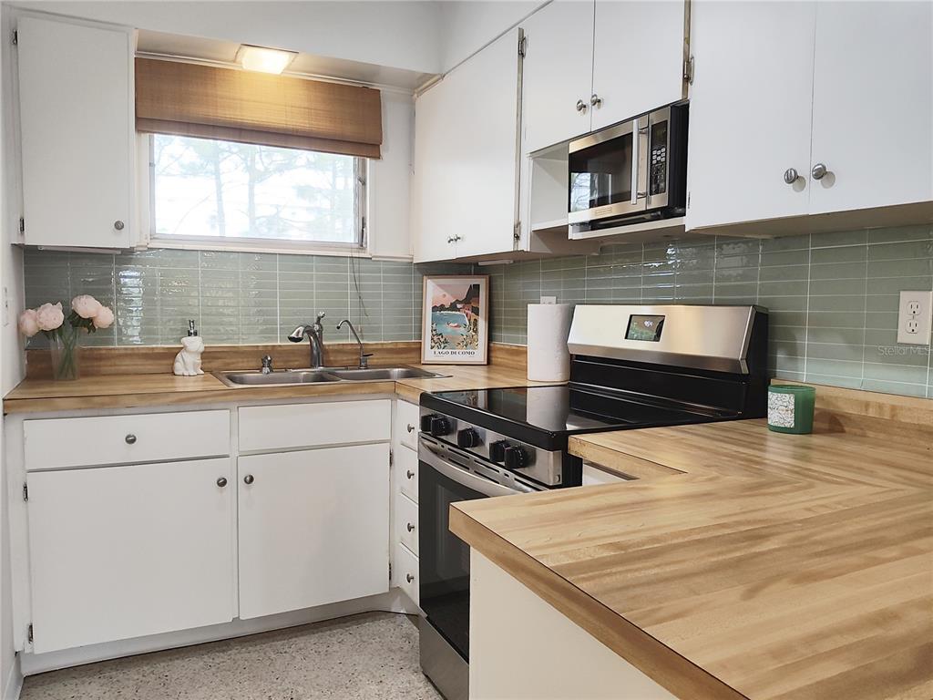 A kitchen features white cabinets, light wood countertops, a green tiled backsplash, and stainless appliances — 2155 WOOD STREET UNIT A26, SARASOTA, FL