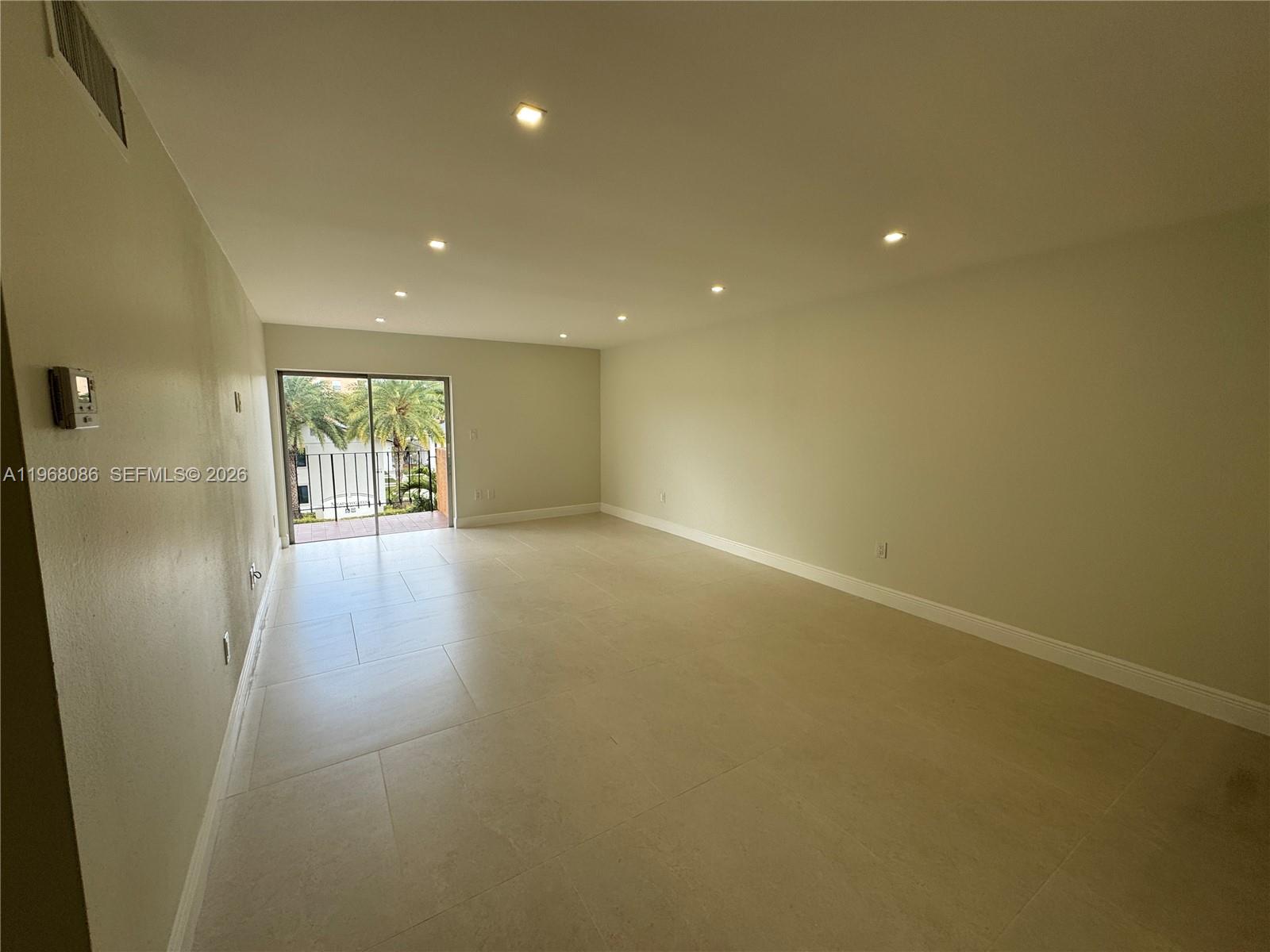 A spacious, empty living room features light-colored tile flooring, recessed lighting, and a sliding glass door — 1900 W 54th St # 219, Hialeah FL 33012, HIALEAH, FL