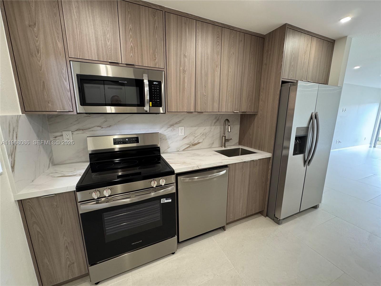 A kitchen features wood-grain cabinets, stainless steel appliances, and white marble-patterned countertops and backsplash — 1900 W 54th St # 219, Hialeah FL 33012, HIALEAH, FL