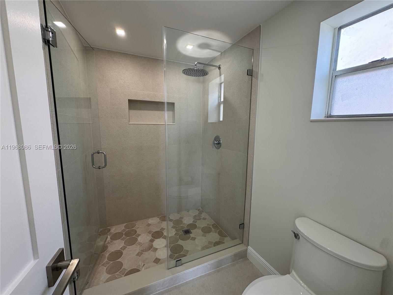 A bathroom features a glass-enclosed walk-in shower with patterned tile flooring and a toilet — 1900 W 54th St # 219, Hialeah FL 33012, HIALEAH, FL