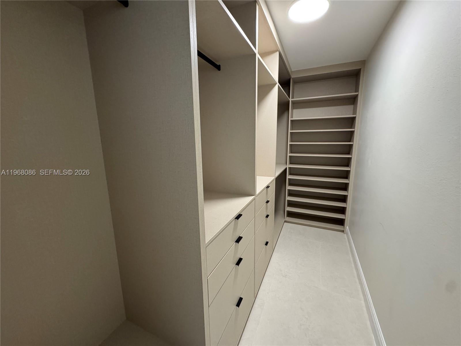 A walk-in closet features custom light-colored shelving, built-in drawers, and tiled flooring — 1900 W 54th St # 219, Hialeah FL 33012, HIALEAH, FL