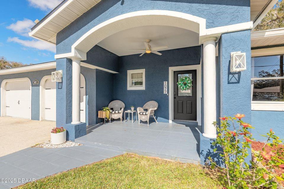 A blue house exterior features a covered front porch with two chairs and a door — 1077 GEORGE ANDERSON STREET, ORMOND BEACH, FL