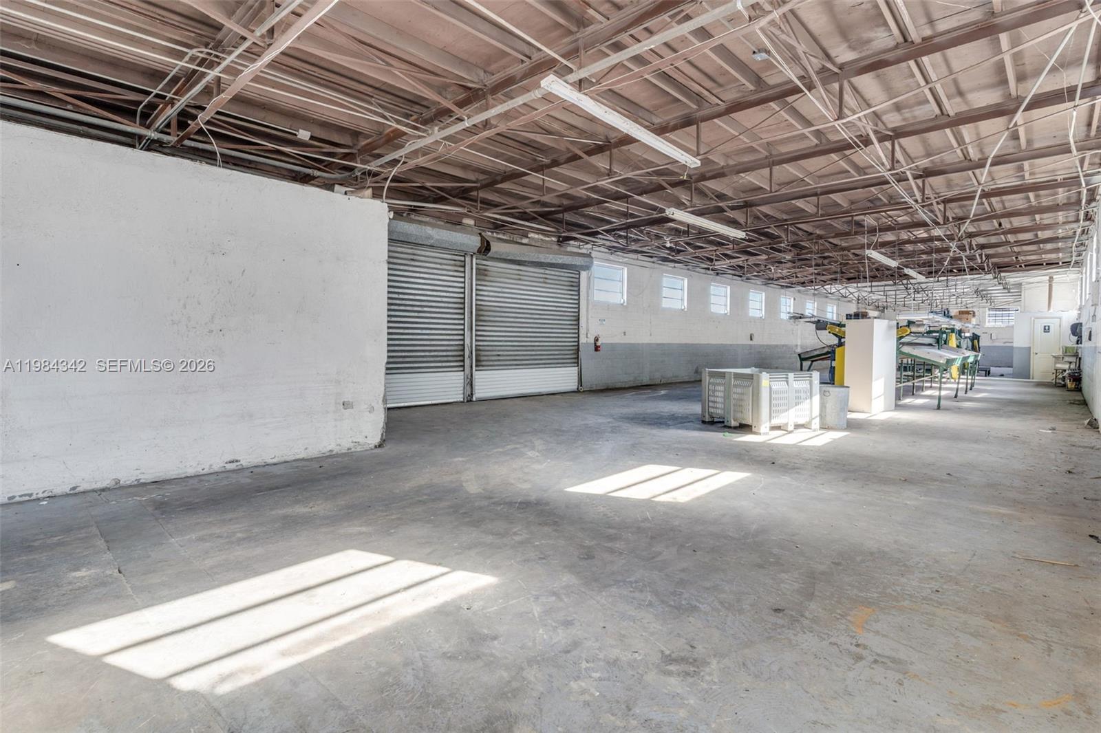 An industrial warehouse space features a concrete floor, exposed ceiling trusses, and roll-up doors — 20601 SW 194th Ave, Miami FL 33187, MIAMI, FL