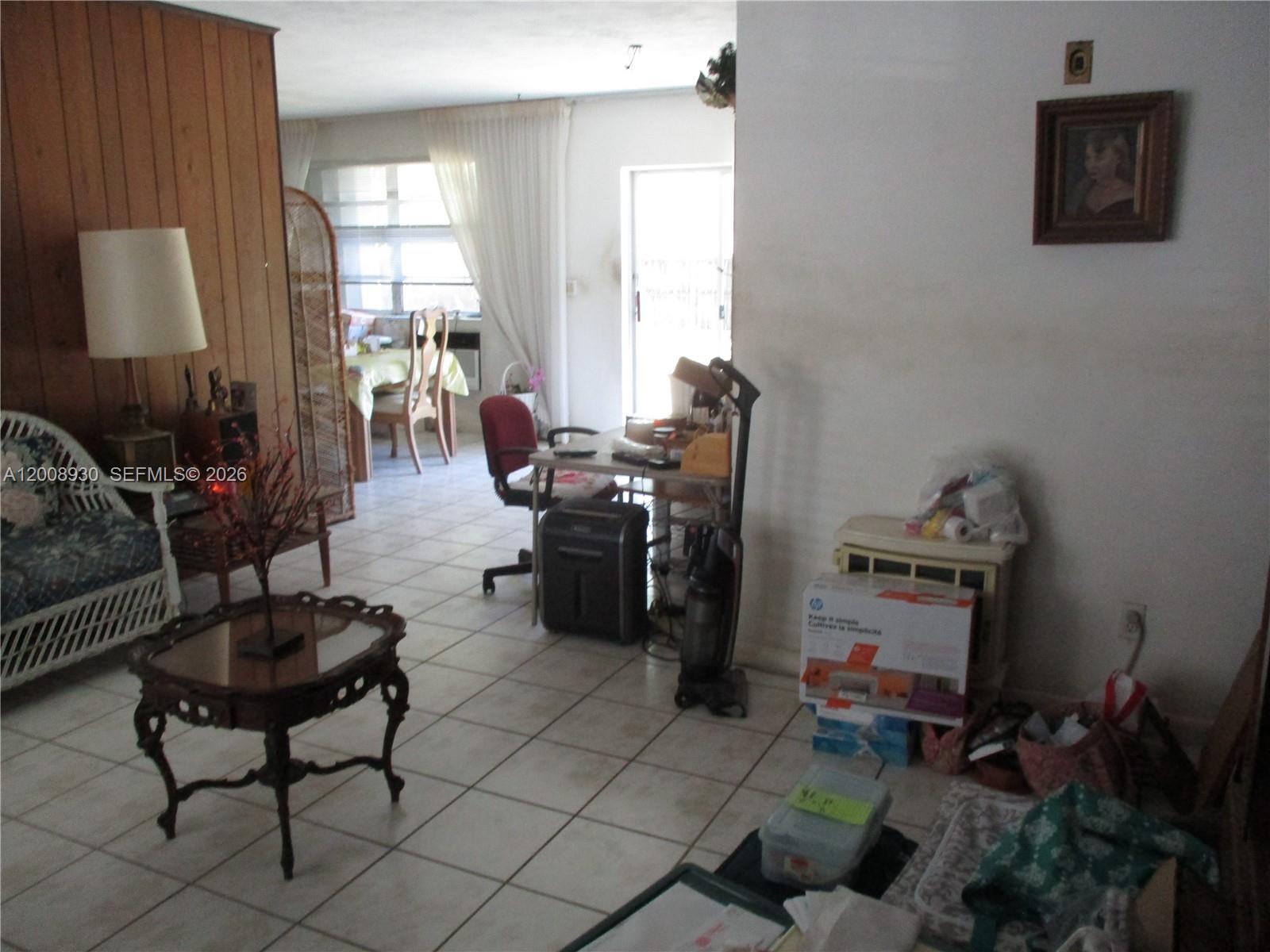 A living room with tile floors, wood-paneled walls, and a dining area in the background — 19311 Gulfstream Rd, Cutler Bay FL 33157, CUTLER BAY, FL