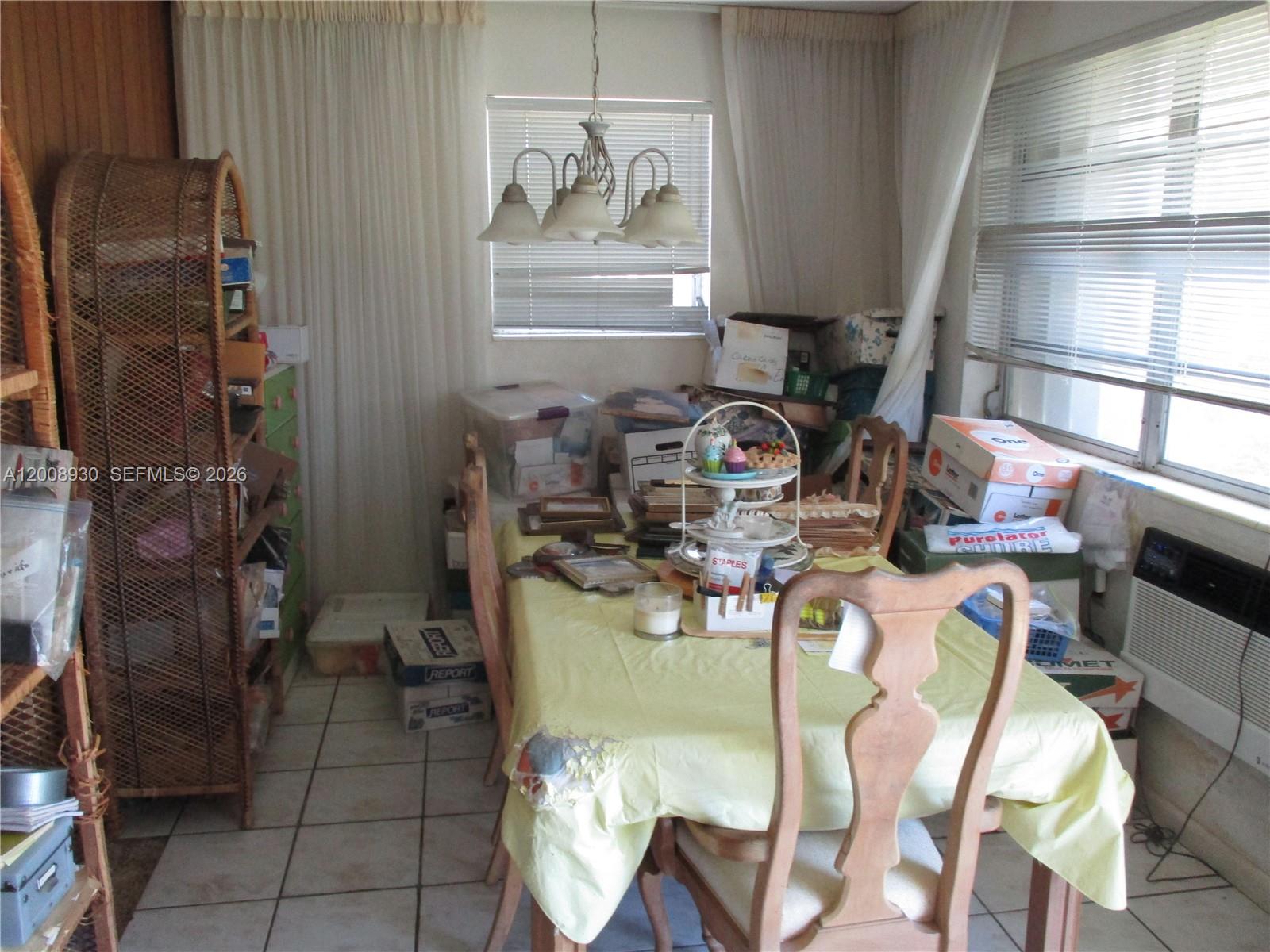 A cluttered dining room features a table with chairs, a wicker shelf, and tile flooring — 19311 Gulfstream Rd, Cutler Bay FL 33157, CUTLER BAY, FL