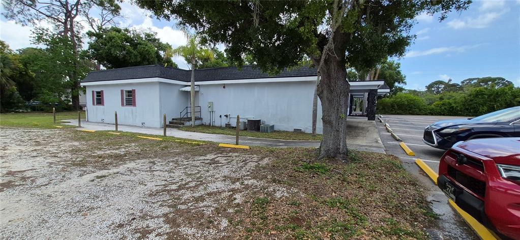 A low-slung, light-colored commercial building features a dark roof, adjacent parking, and mature trees — 7789 131ST STREET N, SEMINOLE, FL